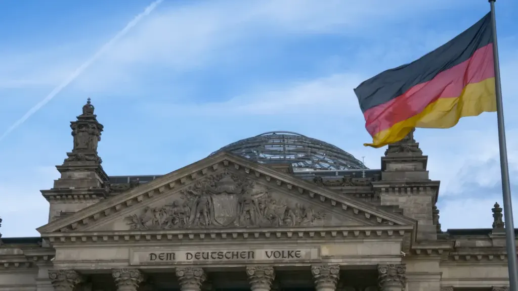Die deutsche Flagge weht vor dem historischen Reichstagsgebäude unter blauem Himmel.
