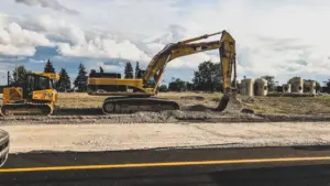 Ein gelber Bagger bei Bauarbeiten neben einer befahrenen Straße bei sonnigem Wetter.