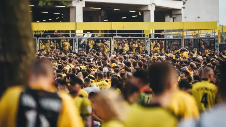 Eine große Menschenmenge in gelben Fußballtrikots vor einem Stadiongebäude in Deutschland.