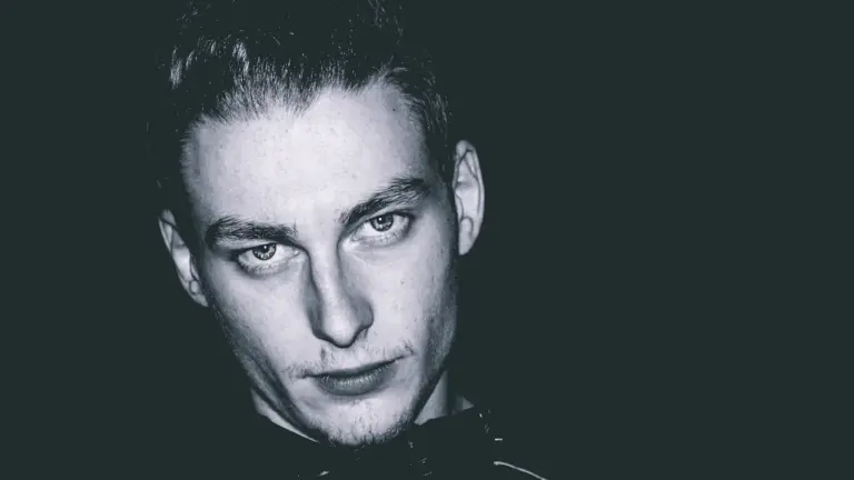 Schwarz-Weiß-Porträt eines jungen Mannes vor dunklem Hintergrund, das an Elvis' Ästhetik erinnert.