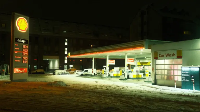 Eine nächtliche Shell-Tankstelle bei Schnee, beleuchtet mit gut sichtbarem Preismast und Zapfsäulen.