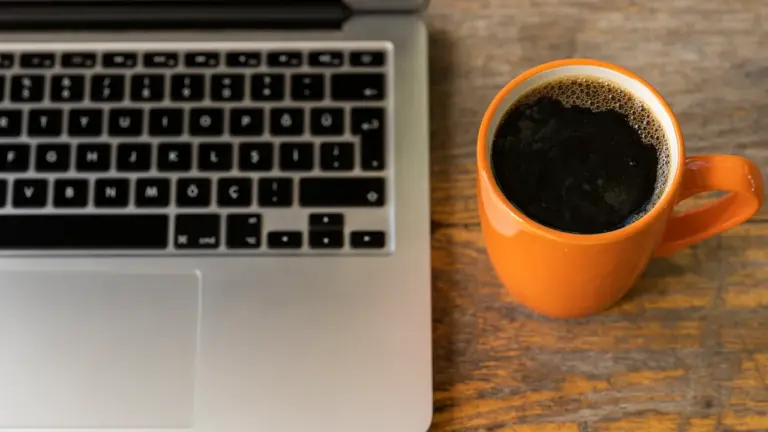 Laptop und eine Tasse Kaffee auf einem Holztisch am Arbeitsplatz.