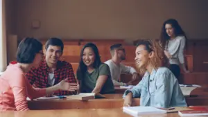 Eine Gruppe junger Studierender sitzt gemeinsam in einem hellen Hörsaal und unterhält sich lebhaft.
