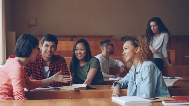 Eine Gruppe junger Studierender sitzt gemeinsam in einem hellen Hörsaal und unterhält sich lebhaft.
