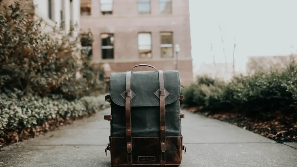 Ein grauer Rucksack steht einsam auf dem Gehweg vor einem alten Schulgebäude.