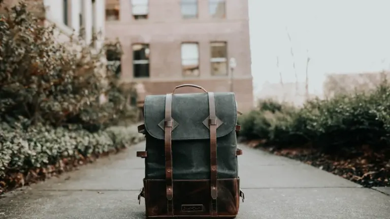 Ein grauer Rucksack steht einsam auf dem Gehweg vor einem alten Schulgebäude.