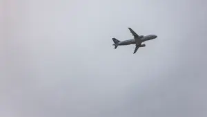 Ein graues Verkehrsflugzeug fliegt am wolkenverhangenen Himmel hoch über der Erde.
