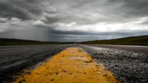 Eine gelbe Fahrbahnmarkierung auf einer nassen Straße unter einem dramatisch bewölkten, stürmischen Himmel.