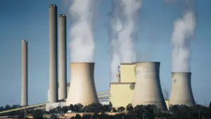 Industrielle Kühltürme stoßen bei blauem Himmel sichtbaren weißen Wasserdampf in die Luft.