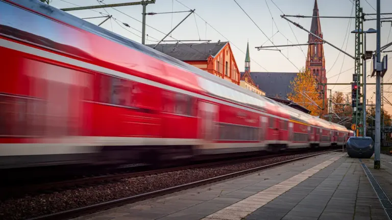 Ein rot-weißer Regionalzug fährt bei Sonnenuntergang in einen Bahnhof in Deutschland ein.