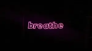 Ein leuchtender, rosa Neon-Schriftzug mit dem englischen Wort Breathe vor dunklem Hintergrund.