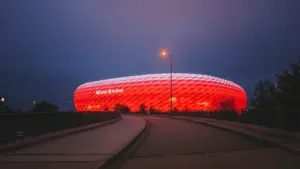 Die rot beleuchtete Allianz Arena bei Nacht unter einem dunklen, stimmungsvollen Münchner Abendhimmel.