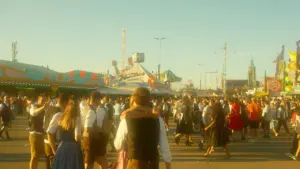 Menschen in traditioneller bayerischer Tracht schlendern über das sonnige Oktoberfestgelände in München.