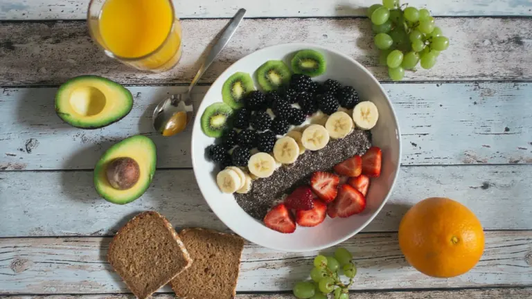 Eine gesunde Frühstücksbowl mit Früchten, Avocado und Vollkornbrot auf einem Holztisch angerichtet.