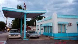 Vintage Tankstelle mit blauem Vordach und alten Autos unter dem hellen Himmel.