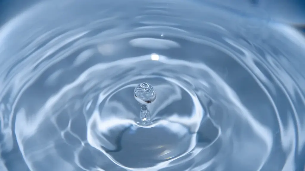 Ein fallender Wassertropfen erzeugt kreisförmige Wellen auf einer blauen Wasseroberfläche.