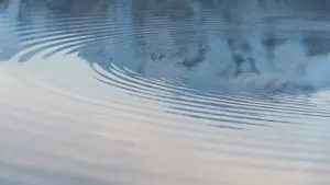 Konzentrische Wellen auf einer ruhigen Wasseroberfläche, die Stille und Bewegung symbolisieren.
