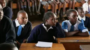 Grundschüler sitzen in einem Klassenzimmer an hölzernen Schultischen beim Unterricht.
