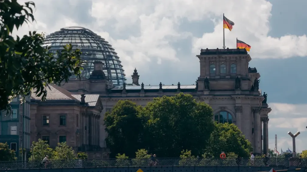 Das Reichstagsgebäude in Berlin mit wehenden deutschen Flaggen bei blauem Himmel.