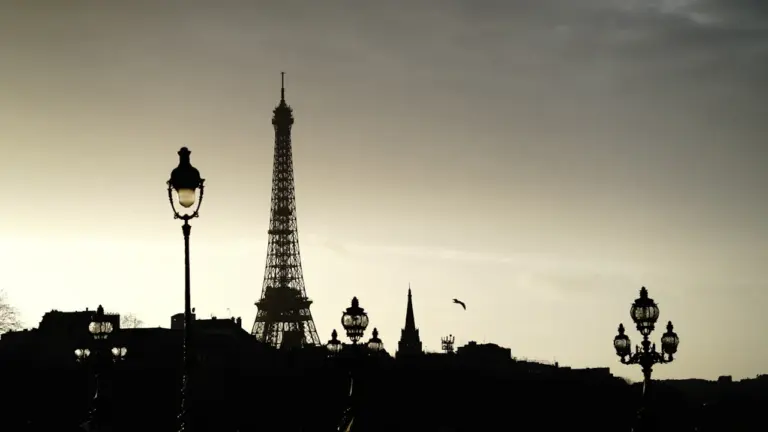 Die Silhouette des Eiffelturms in Paris vor einem stimmungsvollen, leicht bewölkten Abendhimmel.